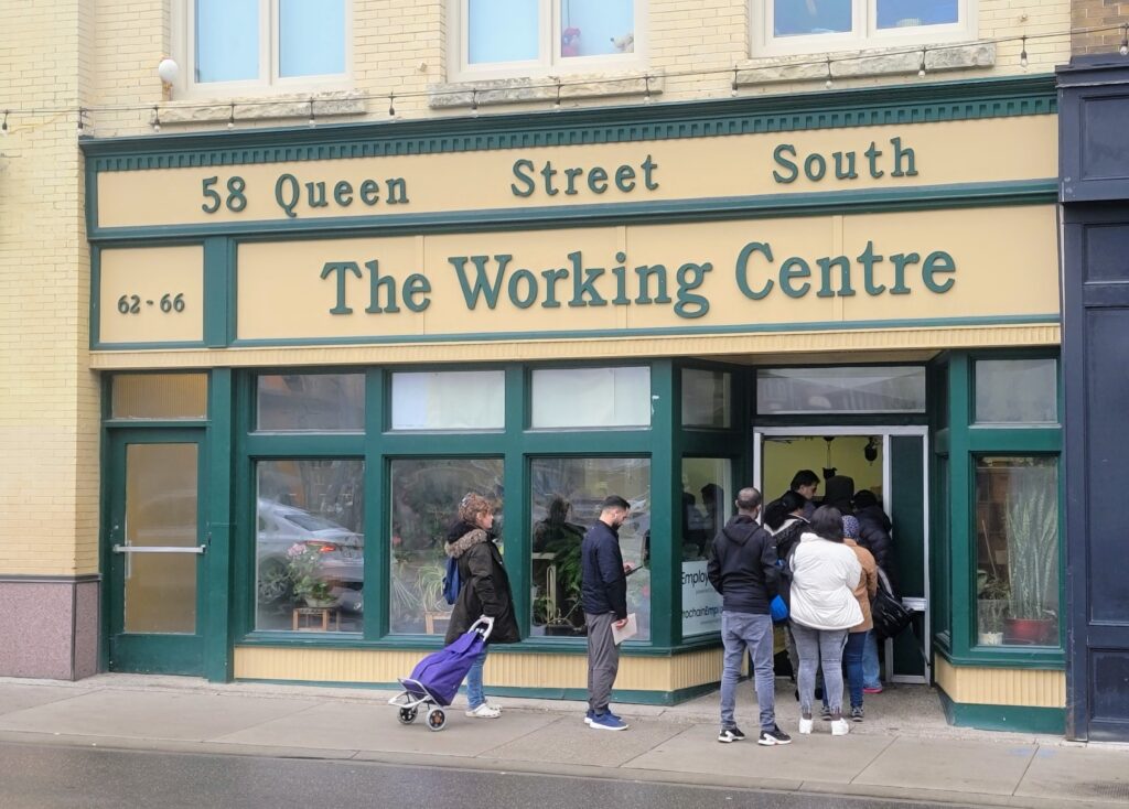 A group of individuals gathered at the entrance of The Working Centre in Kitchener, Ontario.