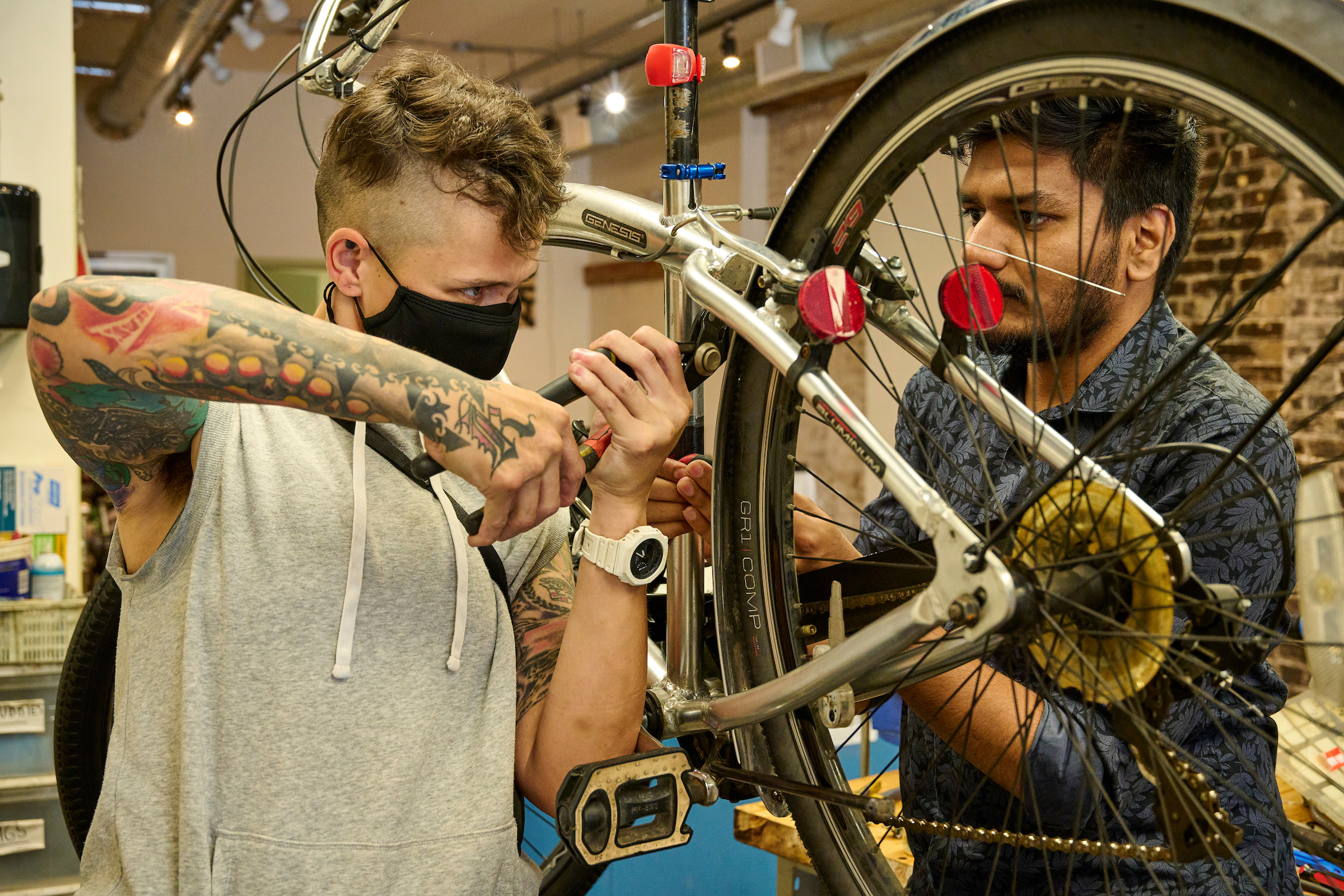 A bike enthusiast and Ani, a staff member at Recycle Cycles in Kitchener, Ontario, collaborate on repairing a bicycle.