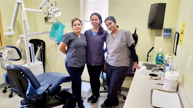 Three volunteers in scrubs smiling at the Community Dental Clinic in Kitchener, Ontario, providing accessible dental care for underserved residents.