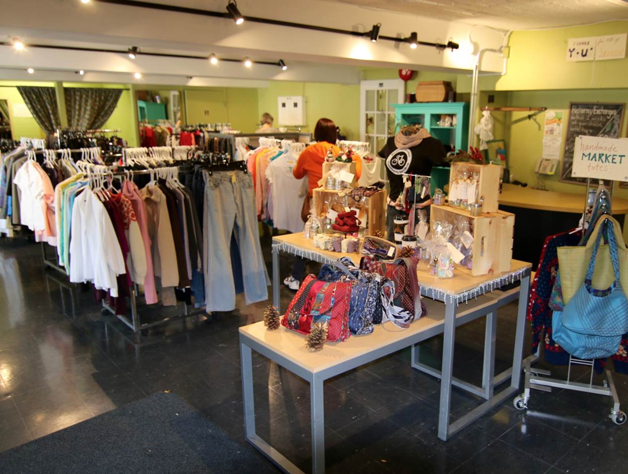 Interior view of The Green Door used clothing store featuring racks of second-hand clothing and tables with accessories.