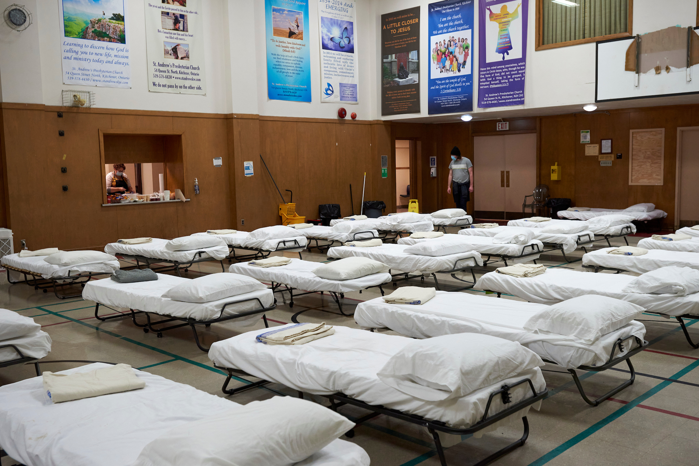 A room with neatly arranged beds and linens at a low-barrier shelter in Kitchener, Ontario, offering safe spaces for individuals experiencing homelessness.