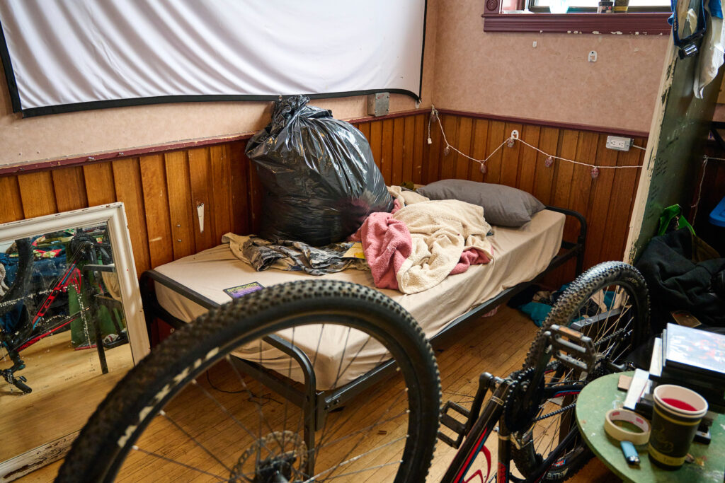 A sleeping space with a bed, personal belongings, and a bicycle in the active area of King Street Shelter, Kitchener, November 22, 2023."