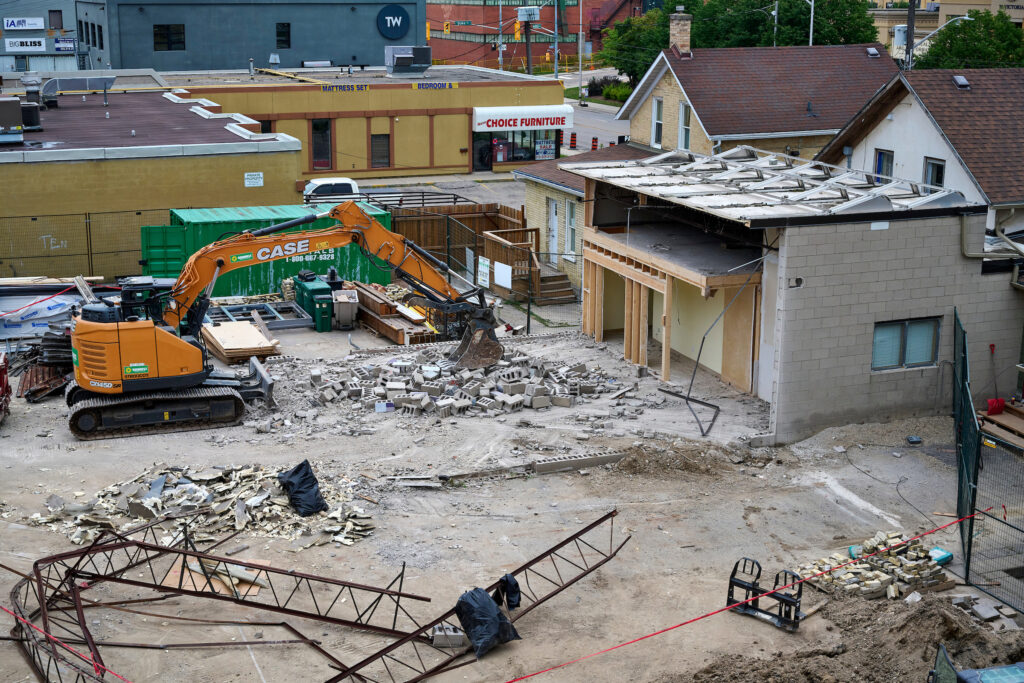 An orange CASE excavator demolishes the garage at 87 Victoria for the Making Home project in Kitchener, Ontario, 2024.