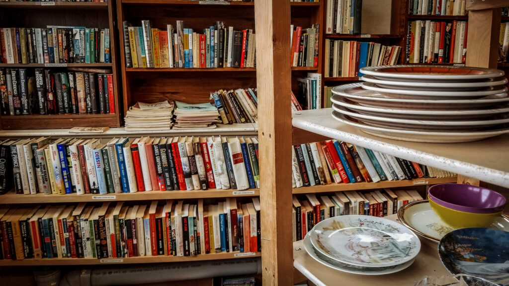 Books neatly arranged on shelves alongside a stack of dishes at Worth a Second Look, a used furniture store in Kitchener, Ontario, 2017.