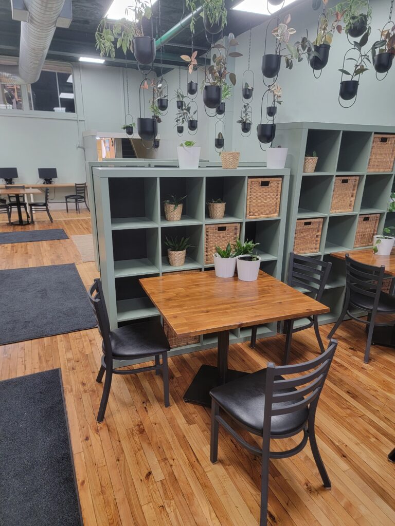 A welcoming community workspace with tables, chairs, and hanging plants at the Job Search Resource Centre in Kitchener, Ontario.