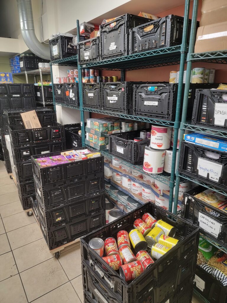 Shelves and crates filled with canned goods and food supplies at the food storage area in Maurita’s Kitchen, Kitchener, Ontario.