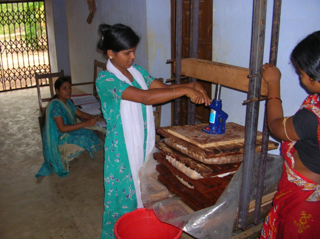 Women in Odisha demonstrating the use of a hydraulic press for processing oilseeds as part of a sustainable biofuel project.