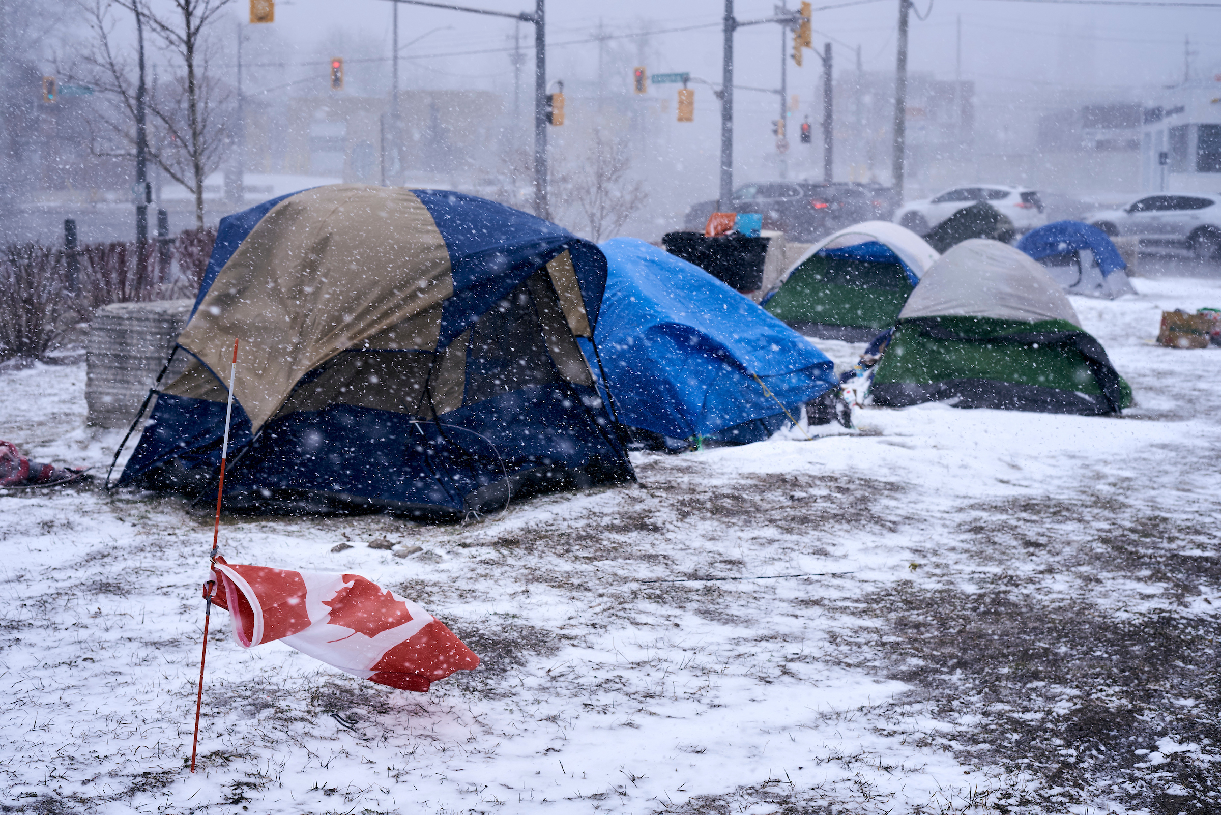 A snowy tent encampment at the intersection of Weber and Victoria Streets in Kitchener, Ontario, active since December 2021, showing multiple tents and a Canadian flag.