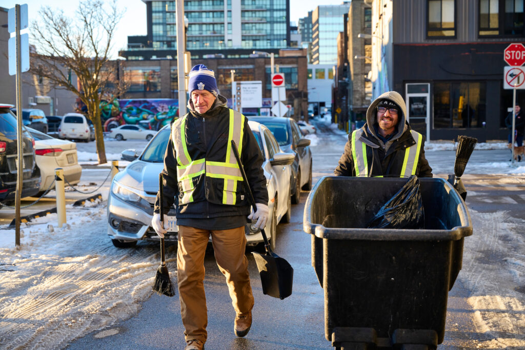 Members of the Clean Team in Kitchener, Ontario, working to keep the downtown area clean during winter, equipped with reflective vests and cleaning tools.