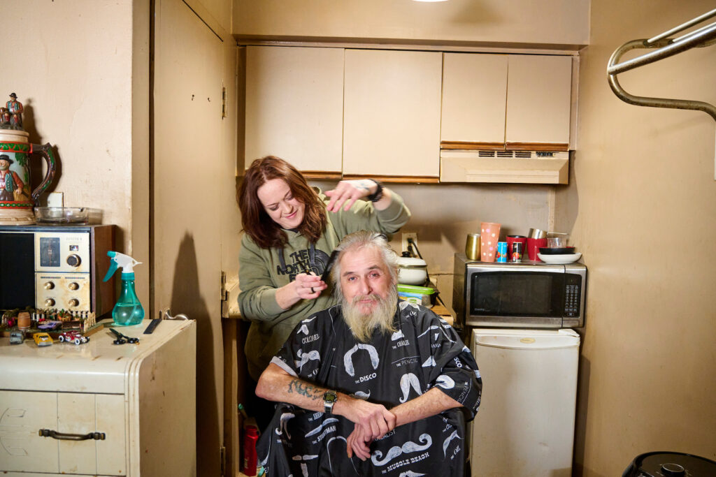 Becca, an SOS outreach worker, provides Ed, a client, with a haircut in his motel room in Kitchener, Ontario.