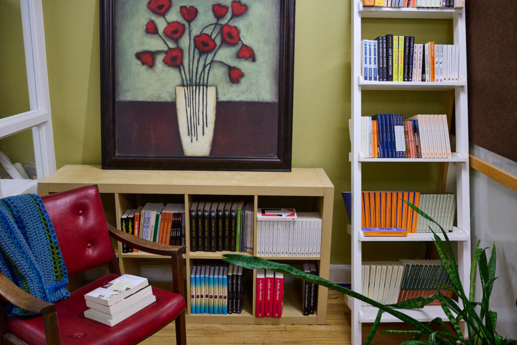 A cozy corner with bookshelves displaying a variety of titles on themes like sustainability and community living at The Working Centre administrative office in Kitchener, Ontario.