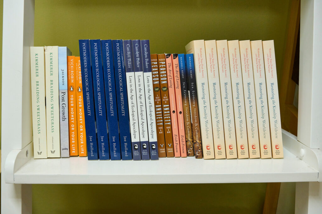 A neatly organized bookshelf displaying titles on ecological spirituality, sustainable living, and cultural reflection at The Working Centre in Kitchener, Ontario.