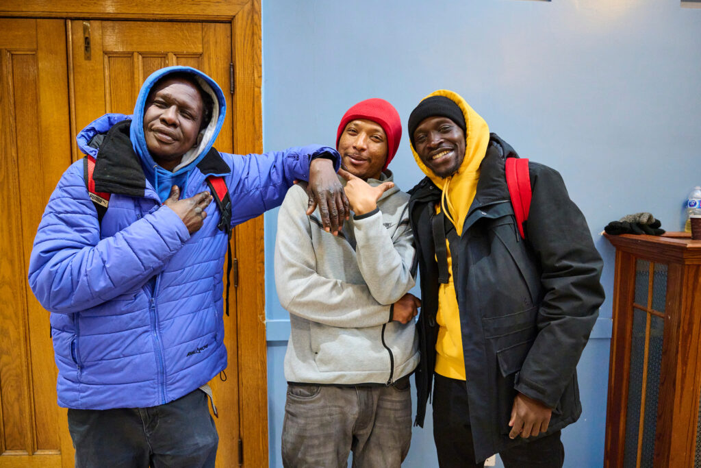 Rambrand, Johannes, and outreach worker Nicholas posing together at St. John’s Kitchen in the St. John the Evangelist Anglican Church, Kitchener, Ontario.