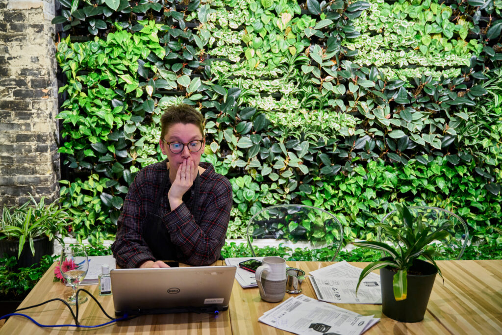 Amy, a staff member, working on her laptop at Fresh Ground Café, Kitchener, Ontario, with a vibrant living wall of greenery in the background.