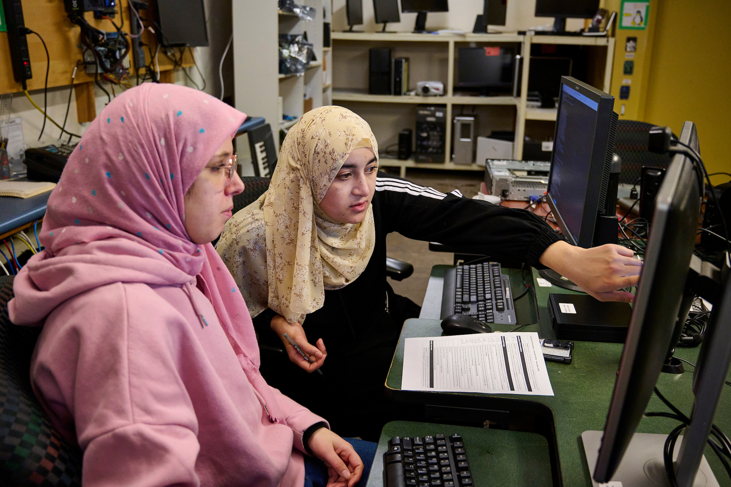 Two women in hijabs working on a desktop computer as part of The Working Centre's Computer Recycling Project in Kitchener, Ontario.