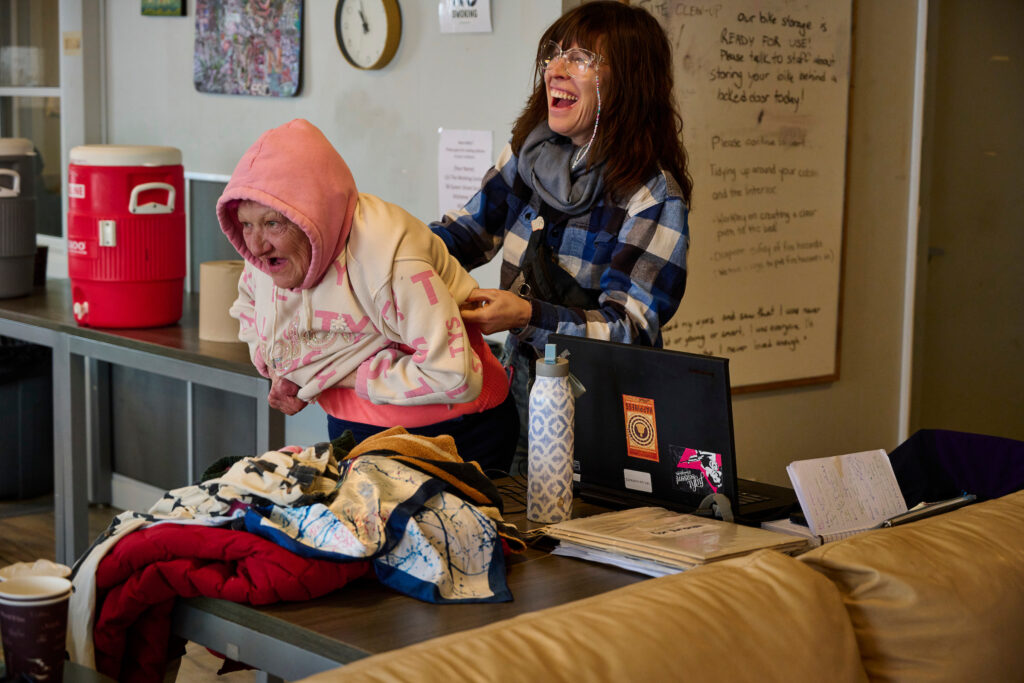 Amanda, a staff member, helps Bunny, a resident, put on her hoodie in the common area of Erbs Road Shelter, a low-barrier shelter in Waterloo, Ontario.