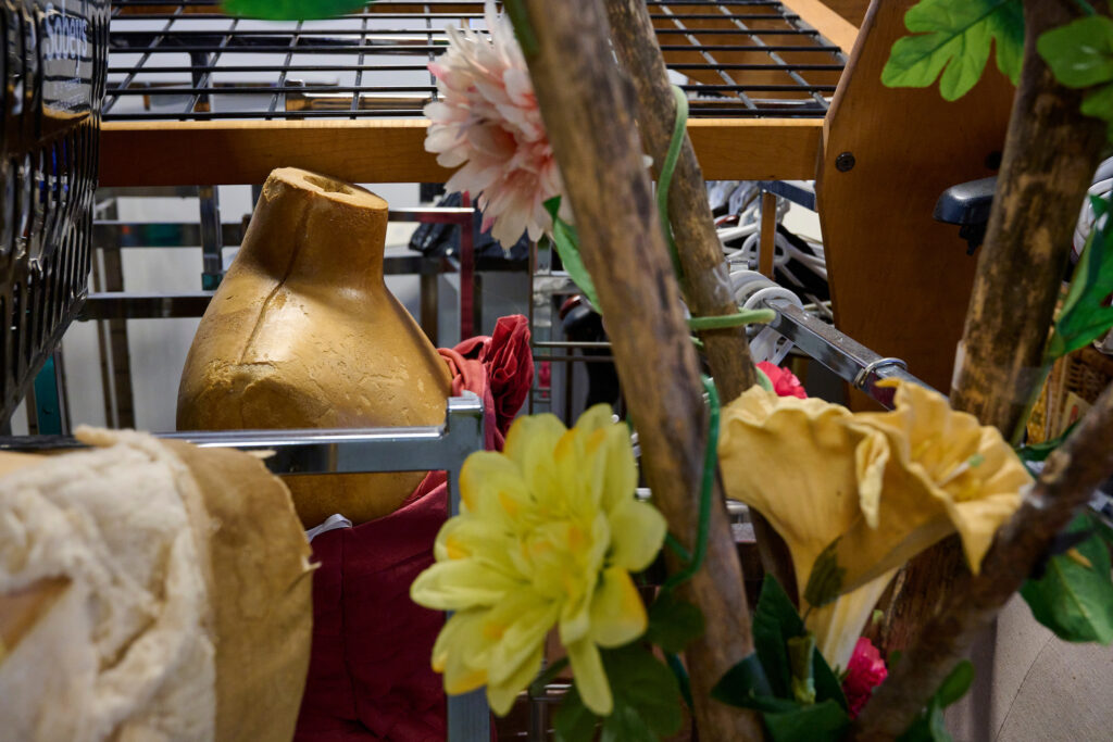 Close-up of a decorative display featuring a mannequin torso, fabric, and artificial flowers at The Green Door used clothing store.