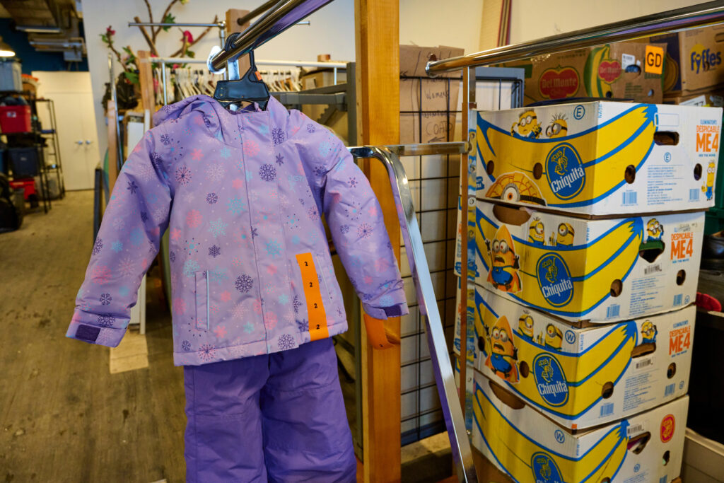 A children’s purple winter jacket on display alongside boxes of donations at The Green Door’s new Queen Street South location, Kitchener, Ontario.